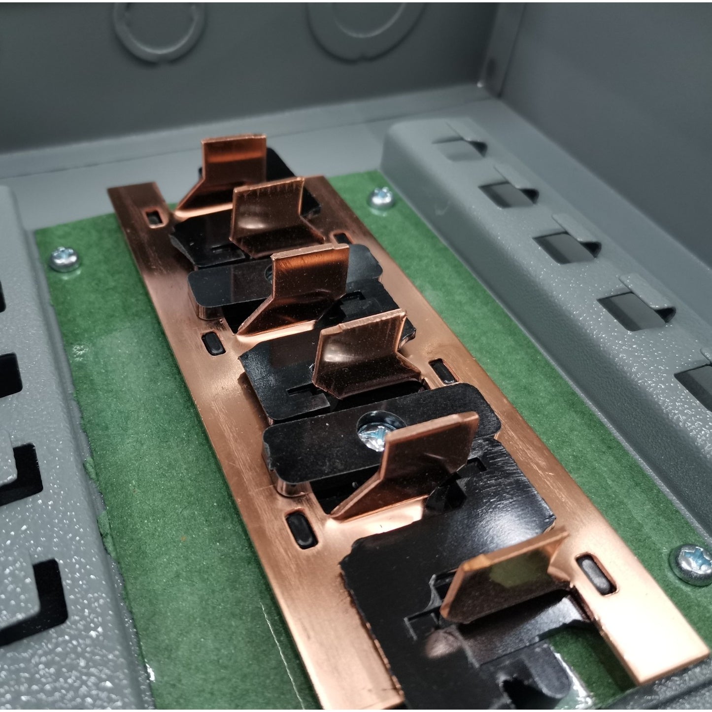 Close-up of a metallic component with copper and black finishes on a green and gray background. America 7X7 Panel Boar 14 Holes Distribution Panel For 2 Pole Plug In Circuit Breaker 12 Branches Side Main