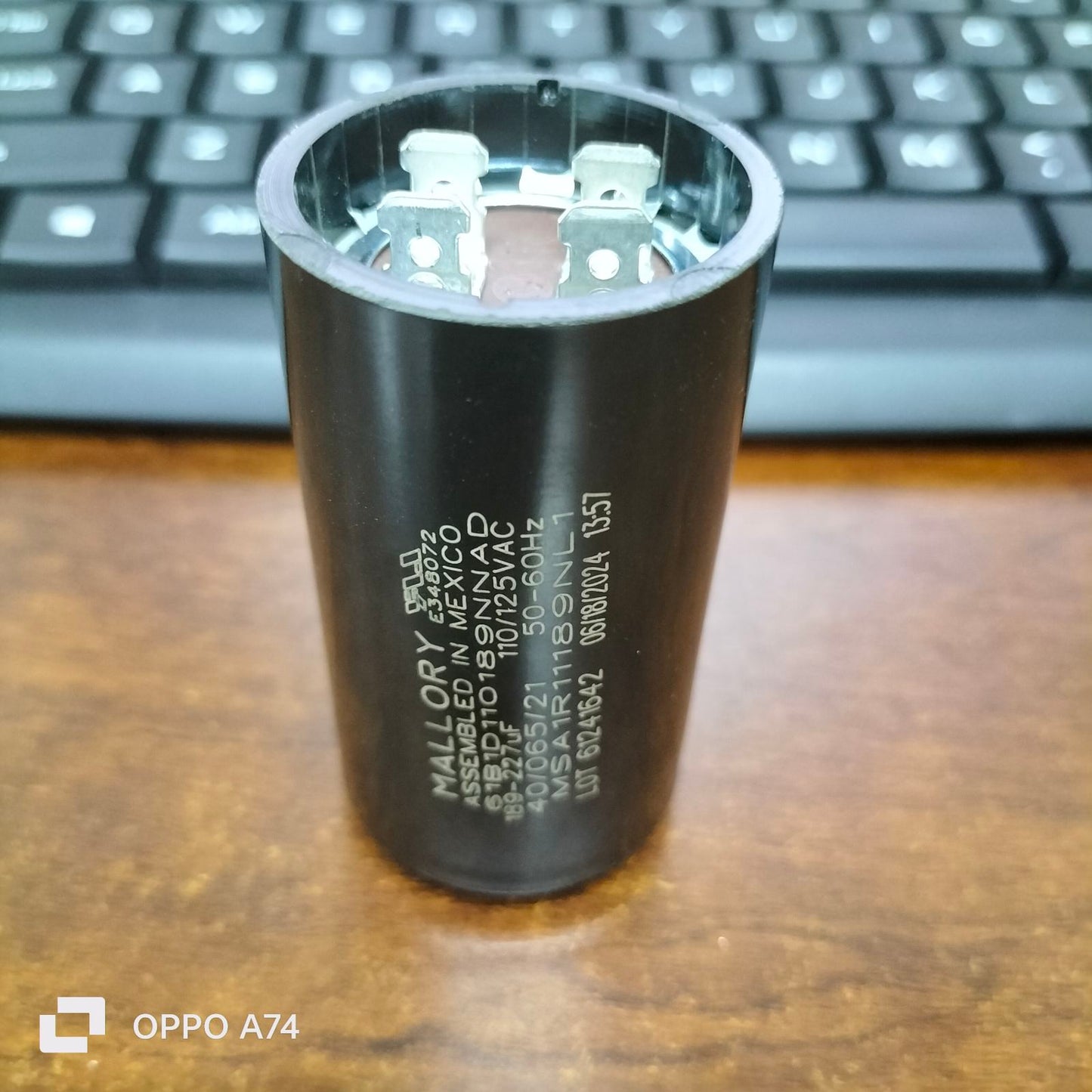 Mallory black Electric Motor Start Capacitor with metal terminals on wooden surface and keyboard background