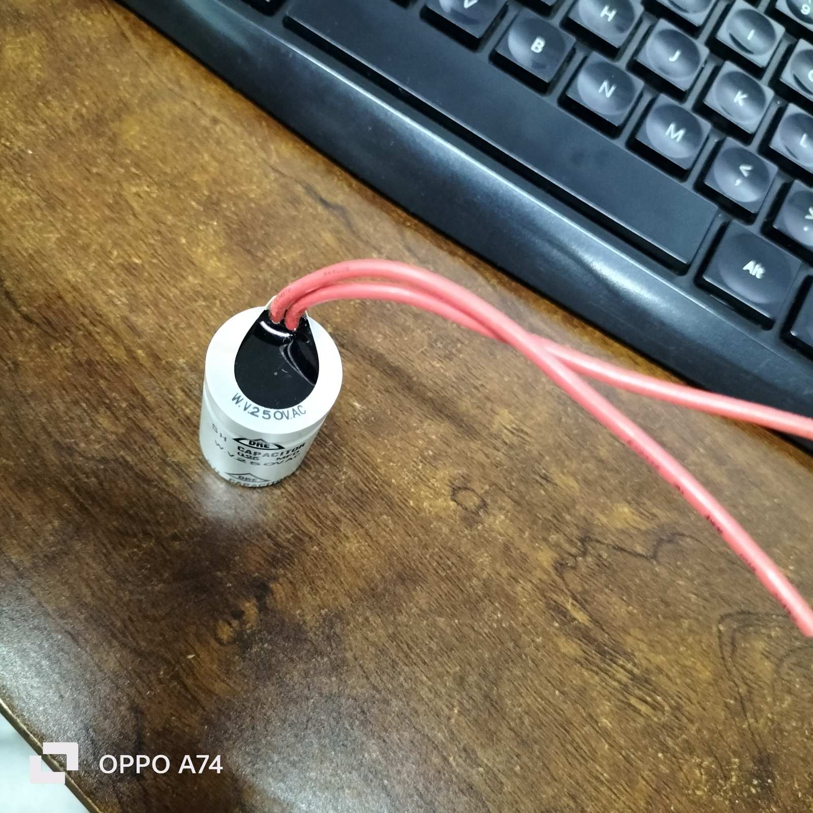 250V capacitor for Motor Parts with red wires on a wooden table next to a keyboard