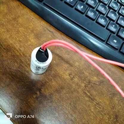 250V capacitor for Motor Parts with red wires on a wooden table next to a keyboard