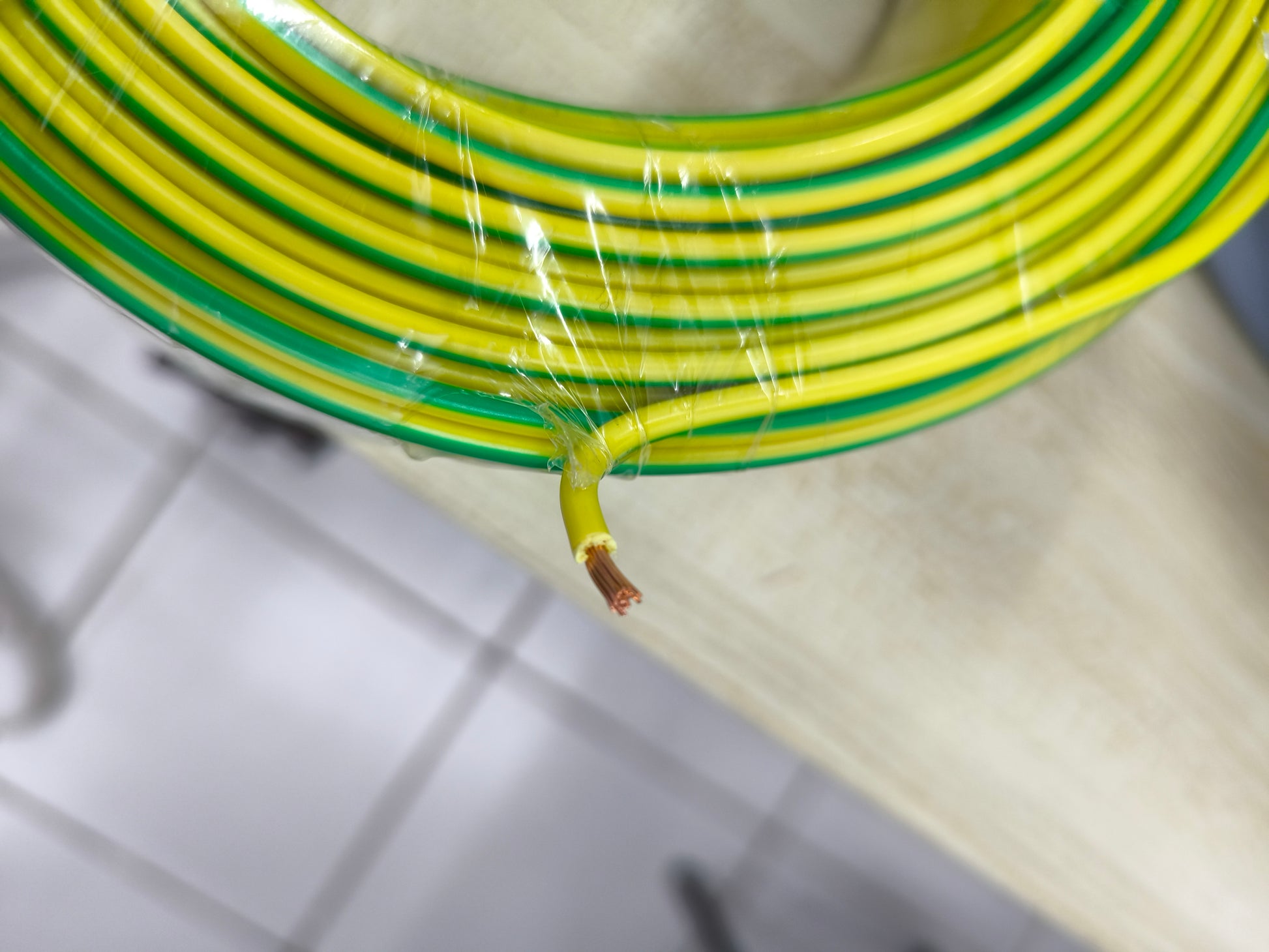 Coiled yellow and green grounding cable 2.0mm AWG14 with exposed copper wire end on a table