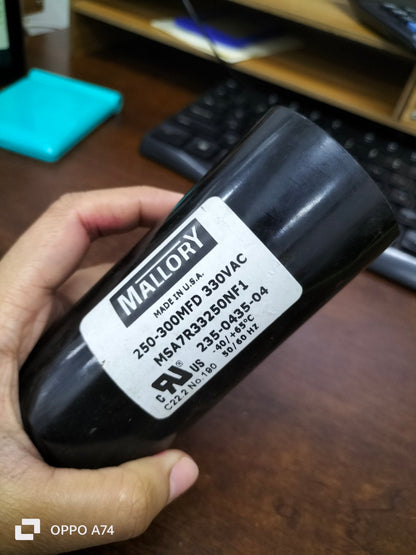 Mallory Capacitor 250-300 MFD 330 VAC electrical circuitry part held in hand on wooden desk