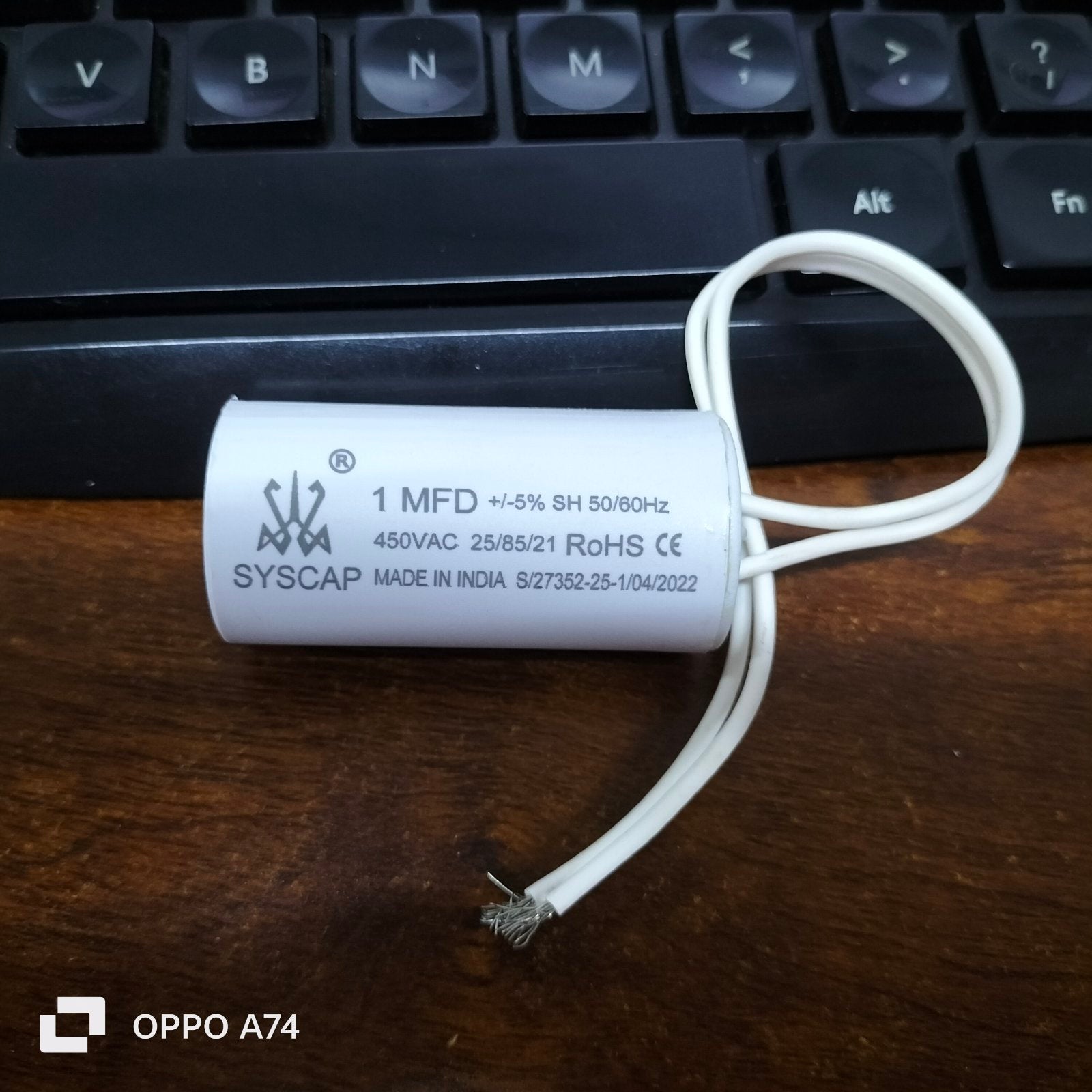 Syscap 1MFD 450V AC Running Capacitor with white wires placed on wooden table near keyboard