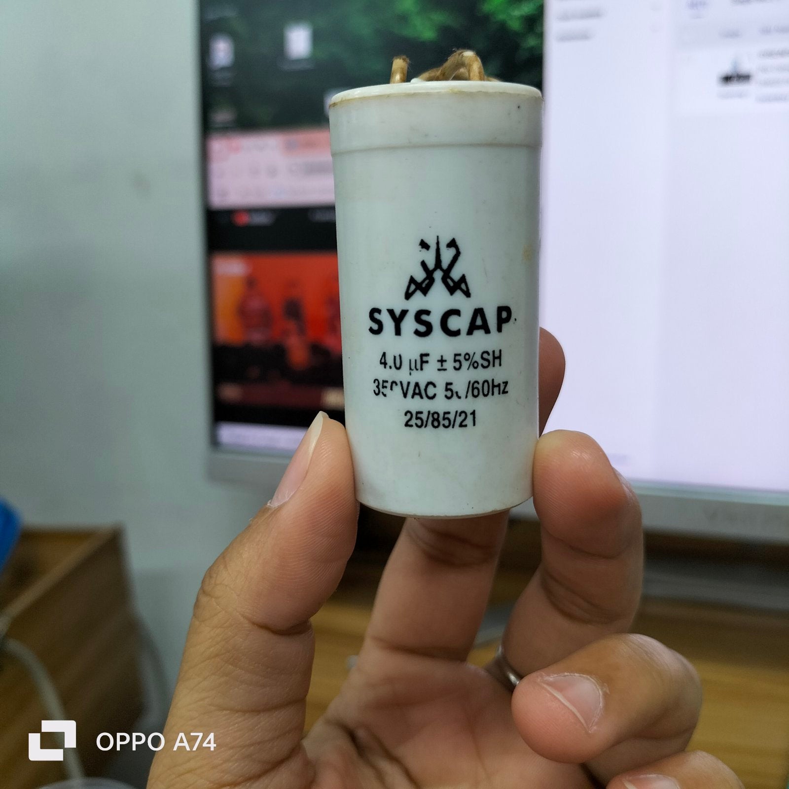Syscap 4MFD Motor Running Capacitor held between fingers with visible specs on white cylindrical body