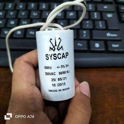 Syscap 5MFD Motor Running Capacitor held in hand with electrical wires and keyboard background
