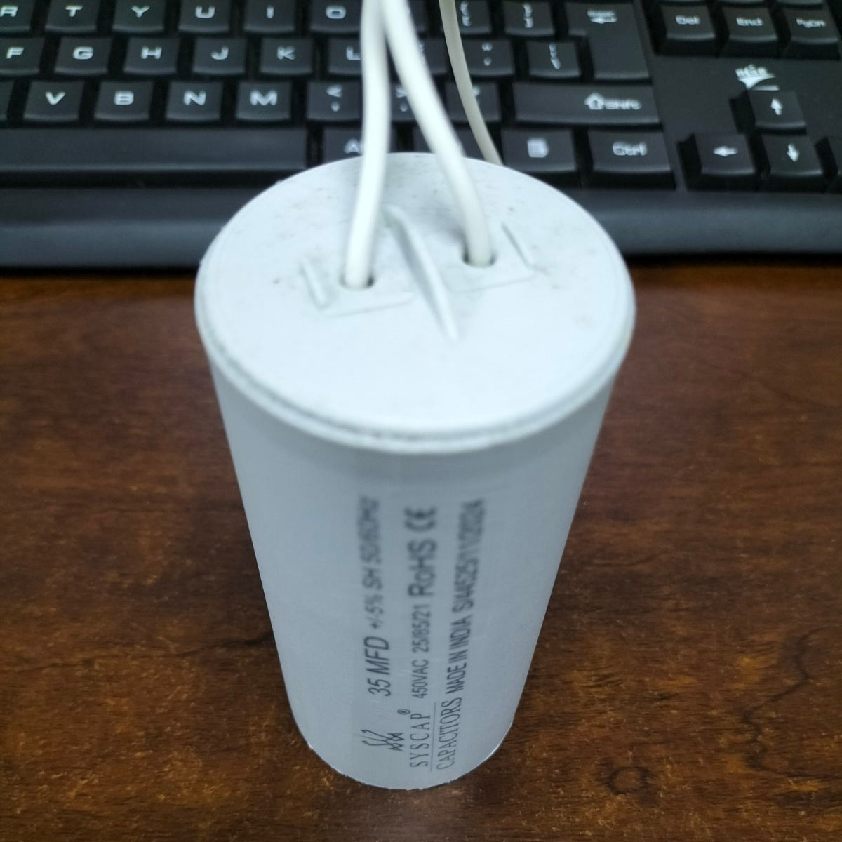 Syscap motor capacitor with white cylindrical body and two attached wires