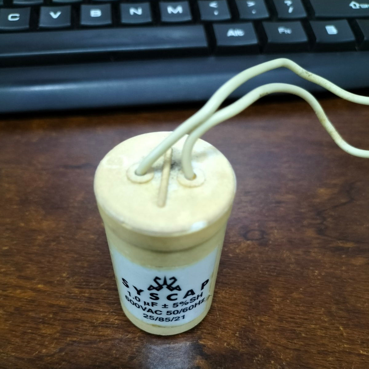 SYSCAP Motor Running Capacitor 1MFD 600V AC cylindrical electrical component with two white wires on wooden surface