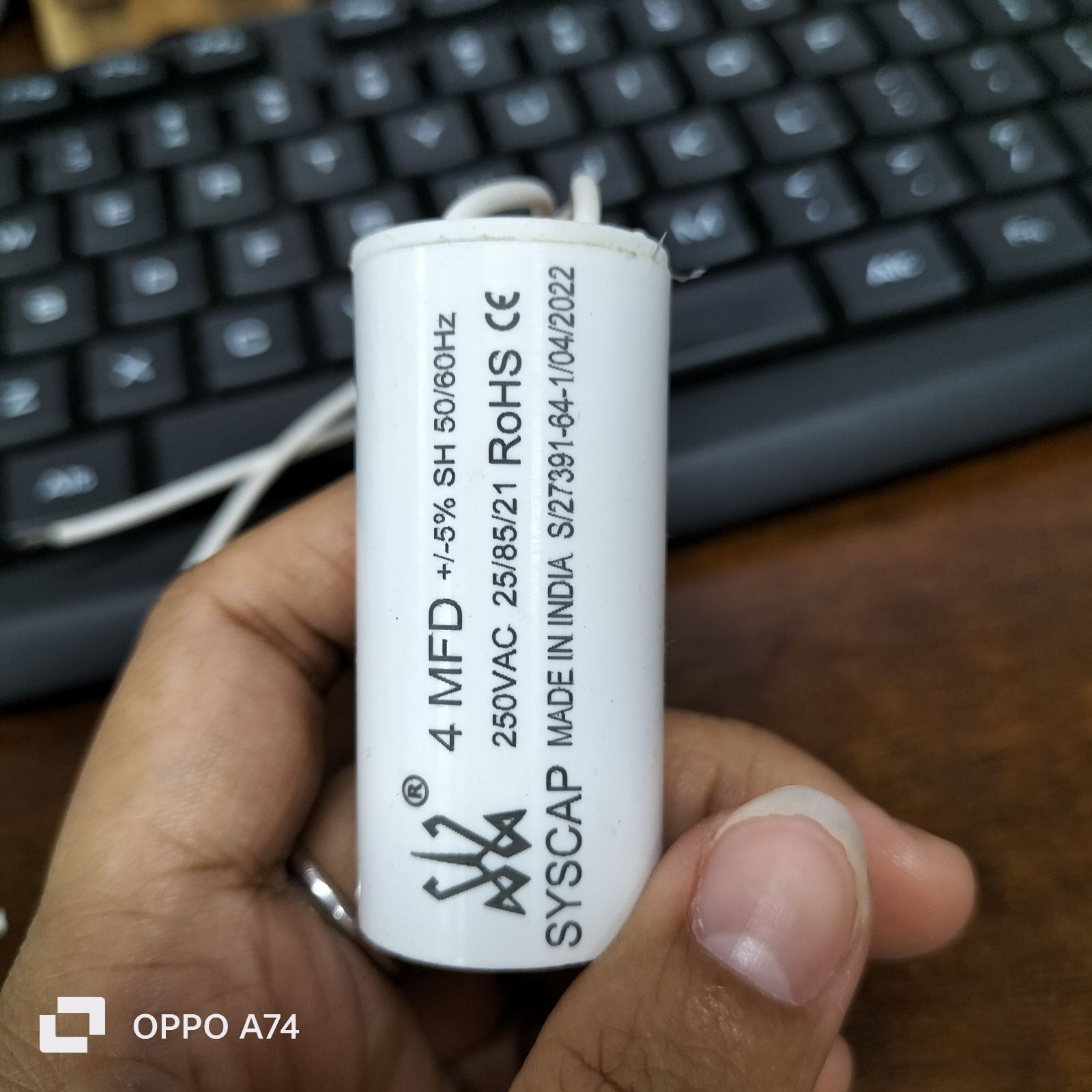 Syscap Running Capacitor 4MFD 250 VAC held in hand with visible specifications on white cylindrical body