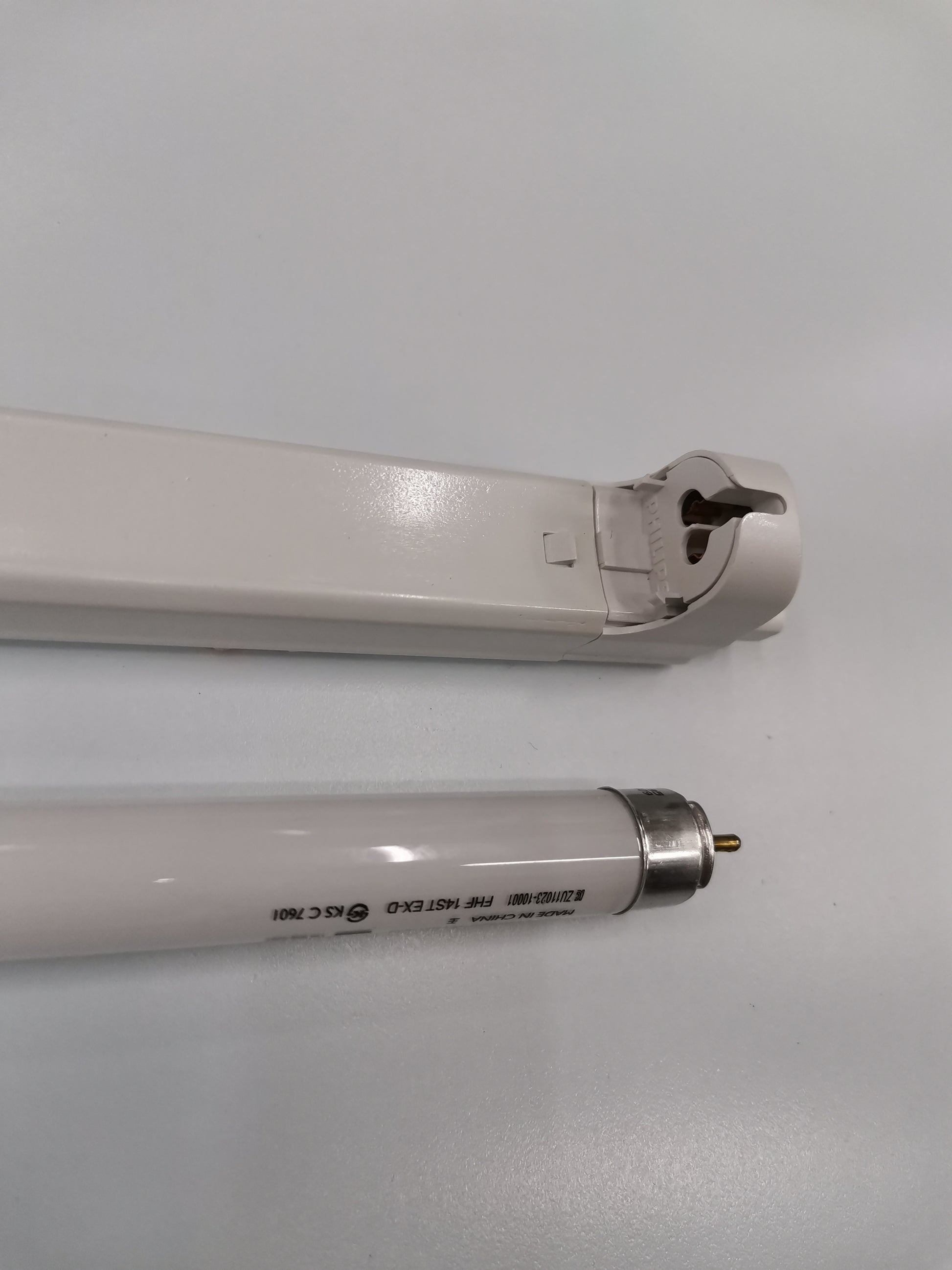 Philips T5 Fluorescent Lamp 28 Watts Daylight tube next to white lamp fixture on a white surface